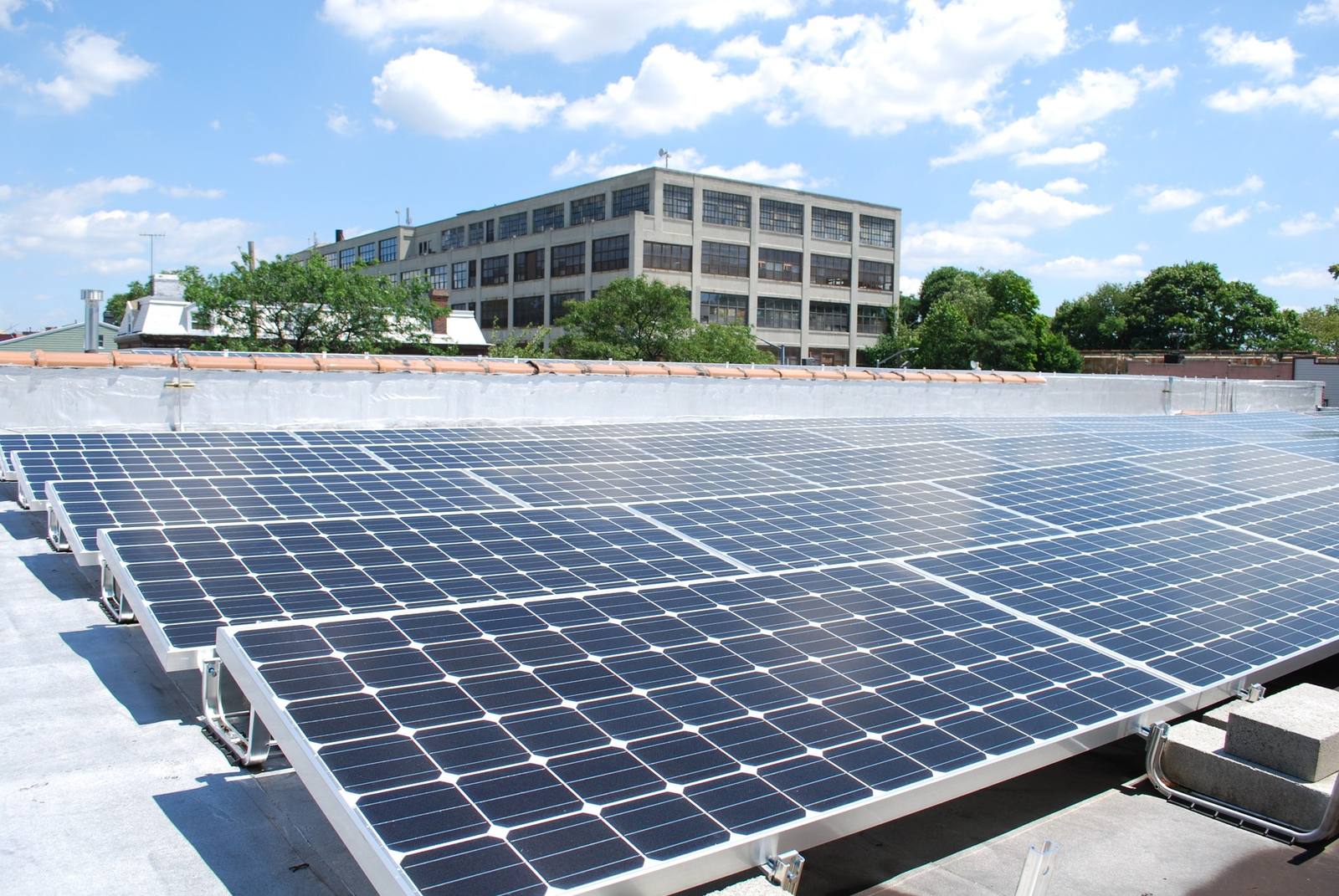 Rows of solar modules on a flat commercial roof, tilted on aluminum frames under a bright sky