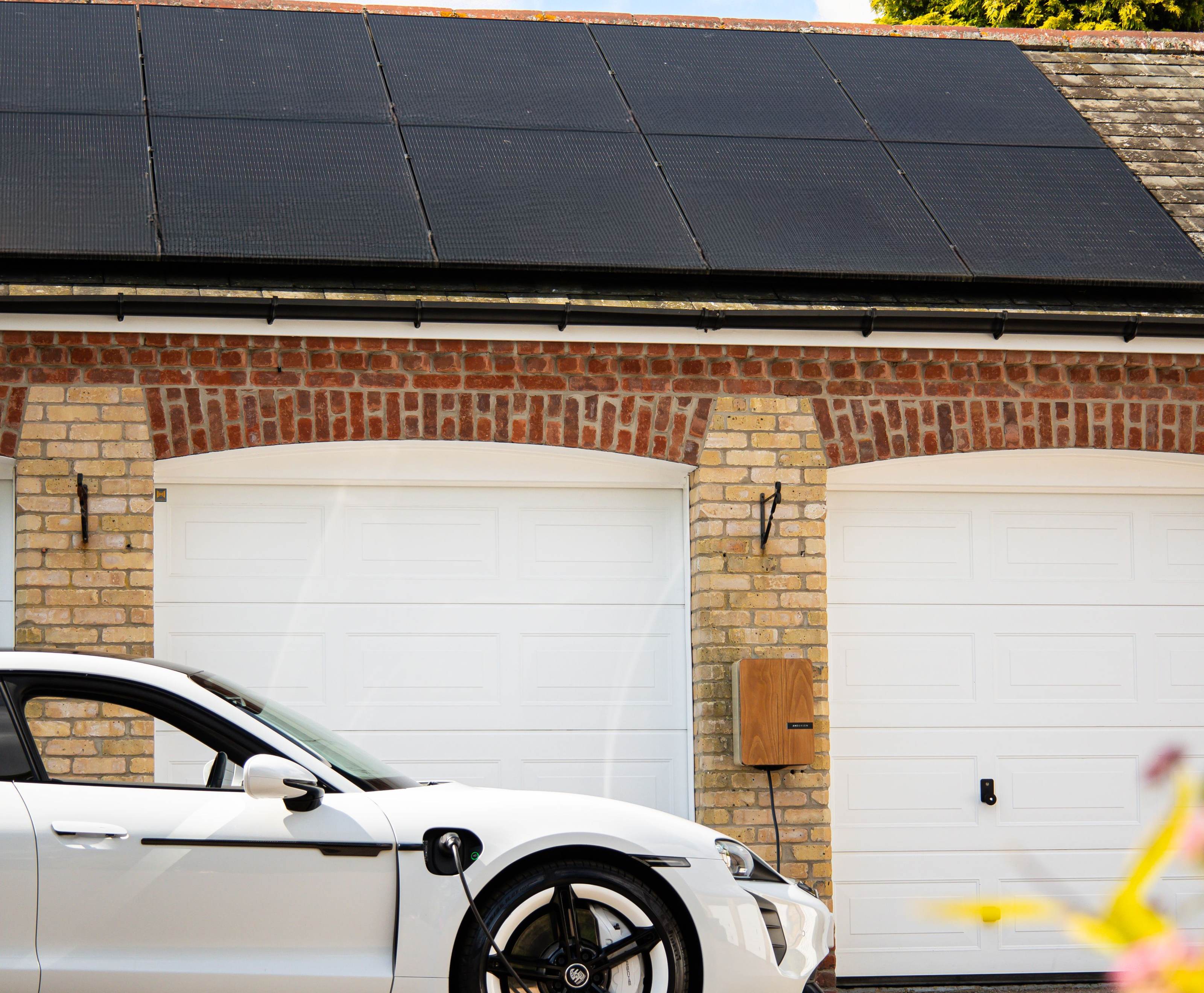Electric car plugged into a home charger with rooftop solar panels and a battery system in the driveway, off-grid power setup