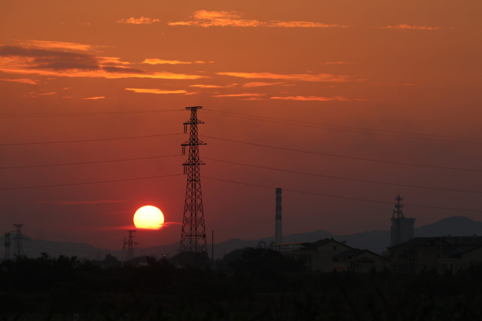 The sun setting directly behind a high-voltage transmission tower and its power lines