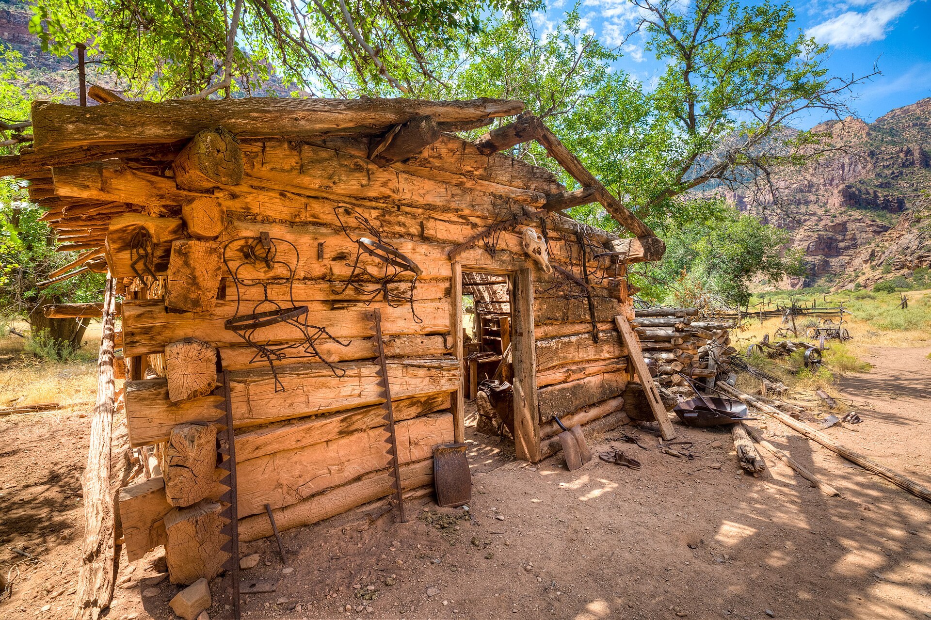 A weathered log cabin with a woodpile and hand tools standing alone in a red-rock canyon