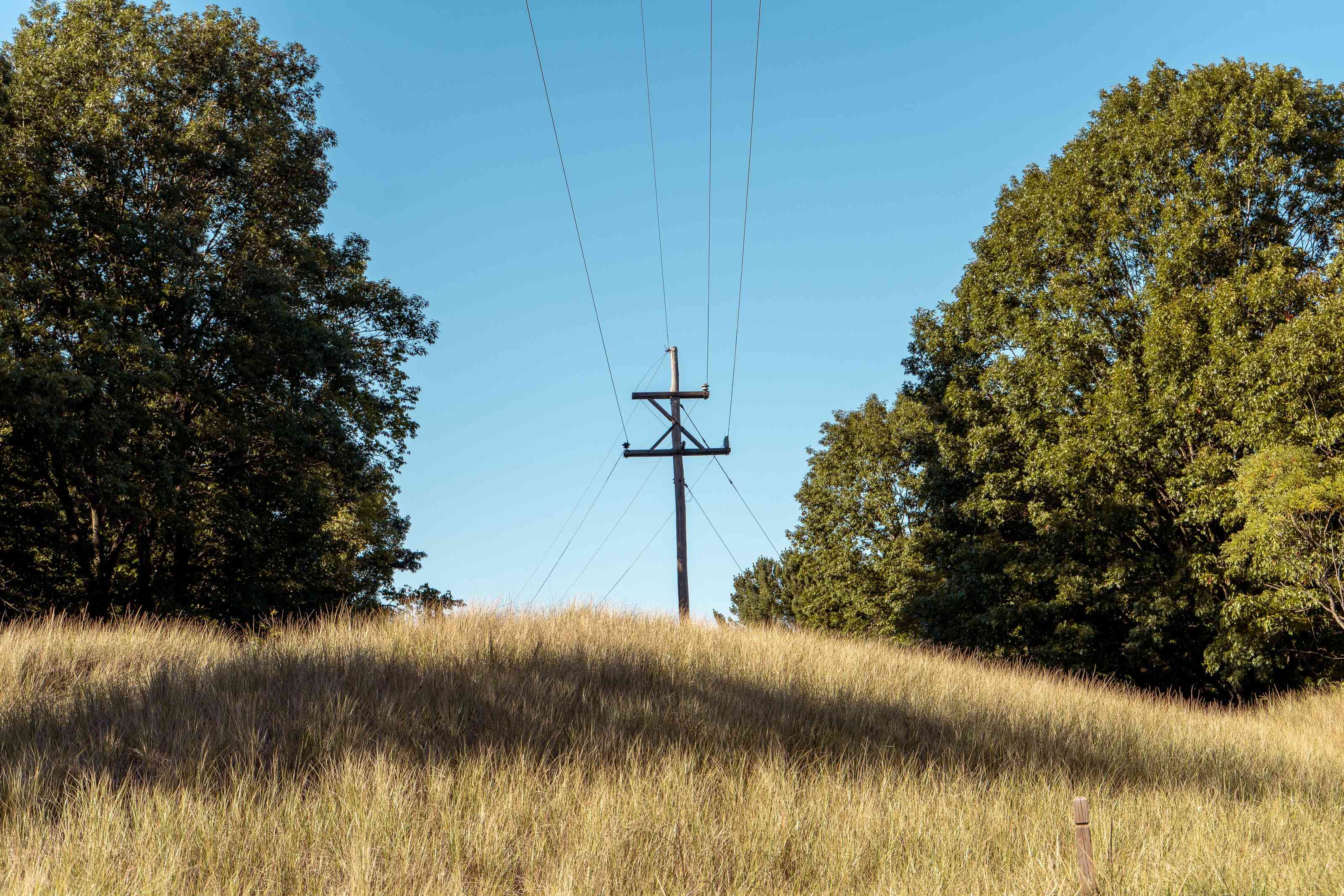 Utility power lines beside a solar-paneled home, illustrating the choice between grid-tied, hybrid and off-grid solar