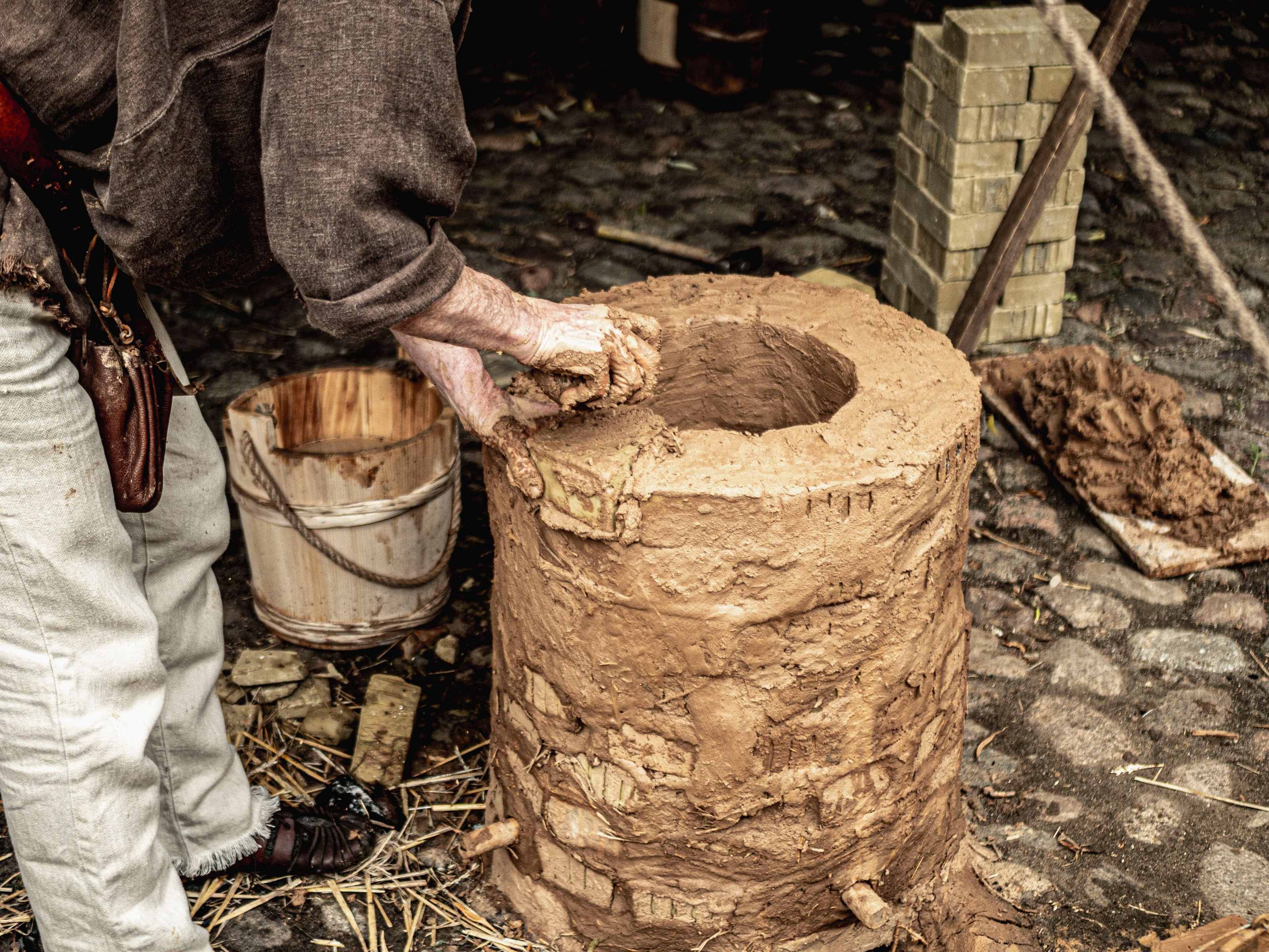 A hand-built rocket mass heater with a curved cob thermal mass bench, steel barrel and firebrick burn tunnel inside an off-grid cabin