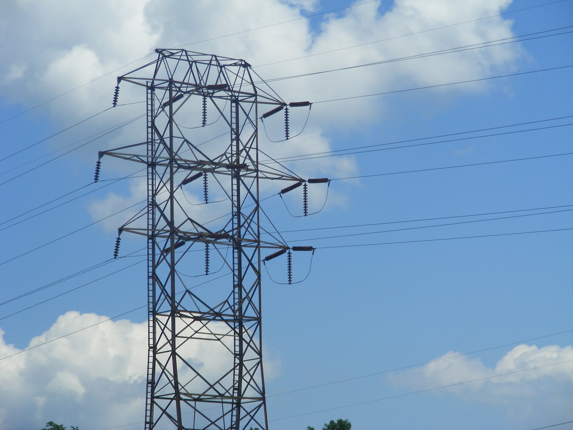 A steel transmission tower and power lines against a summer sky with cumulus clouds