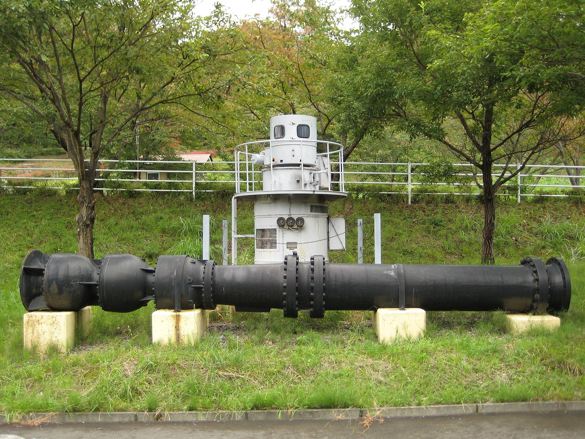 A large water pump and its vertical electric drive motor preserved on a concrete plinth outside a pumping station