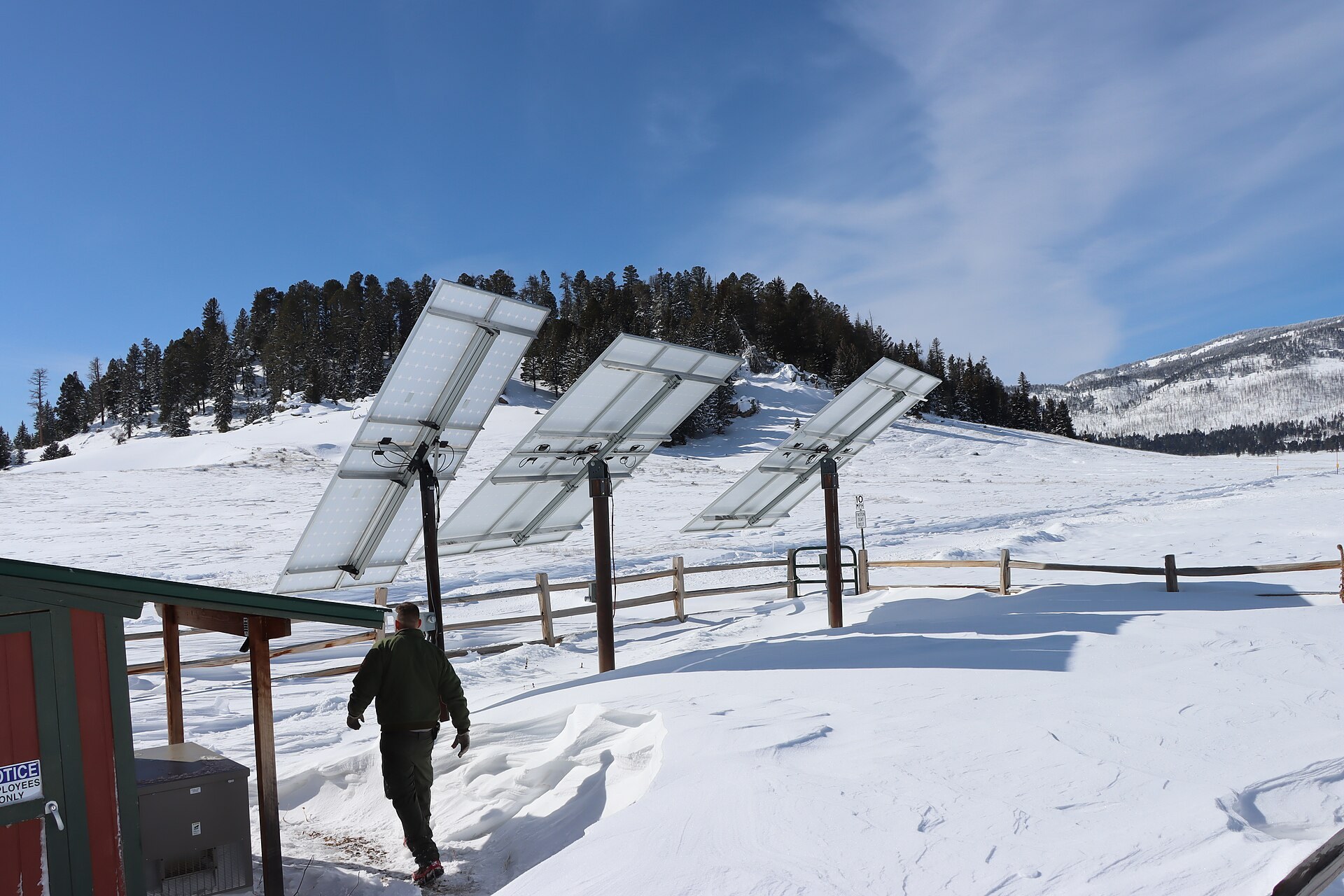 Three steeply tilted pole-mounted solar panels standing clear of deep snow on a mountain meadow under a winter sky